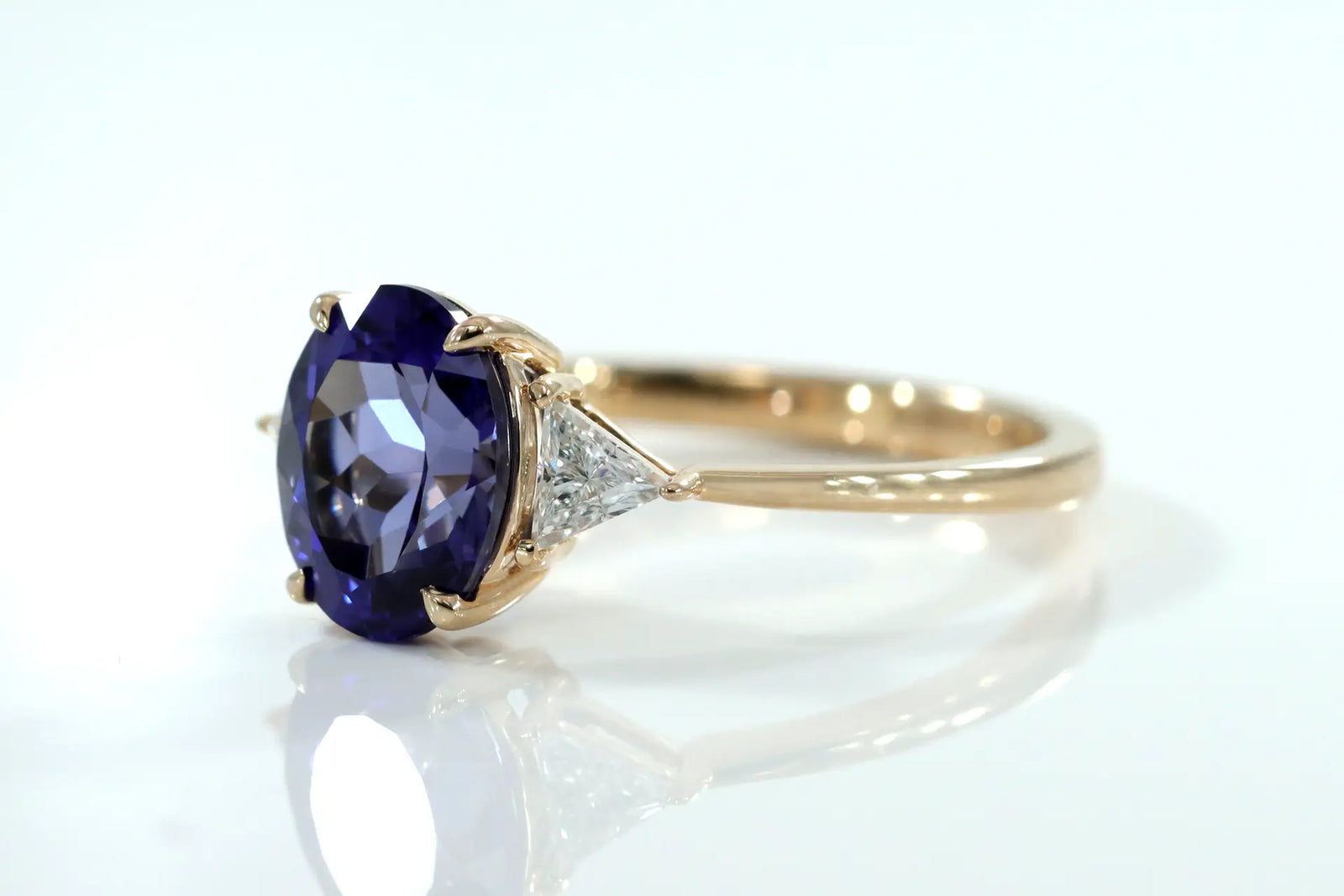 affordable designer claw prong 18k yellow gold three stone 2.5 carat oval lab grown tanzanite with lab diamond triangle sides engagement ring Quorri