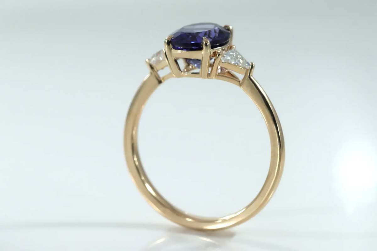 designer 14k yellow gold three stone engagement ring with 2 carat oval lab grown tanzanite center with lab grown diamond triangle sides at Quorri