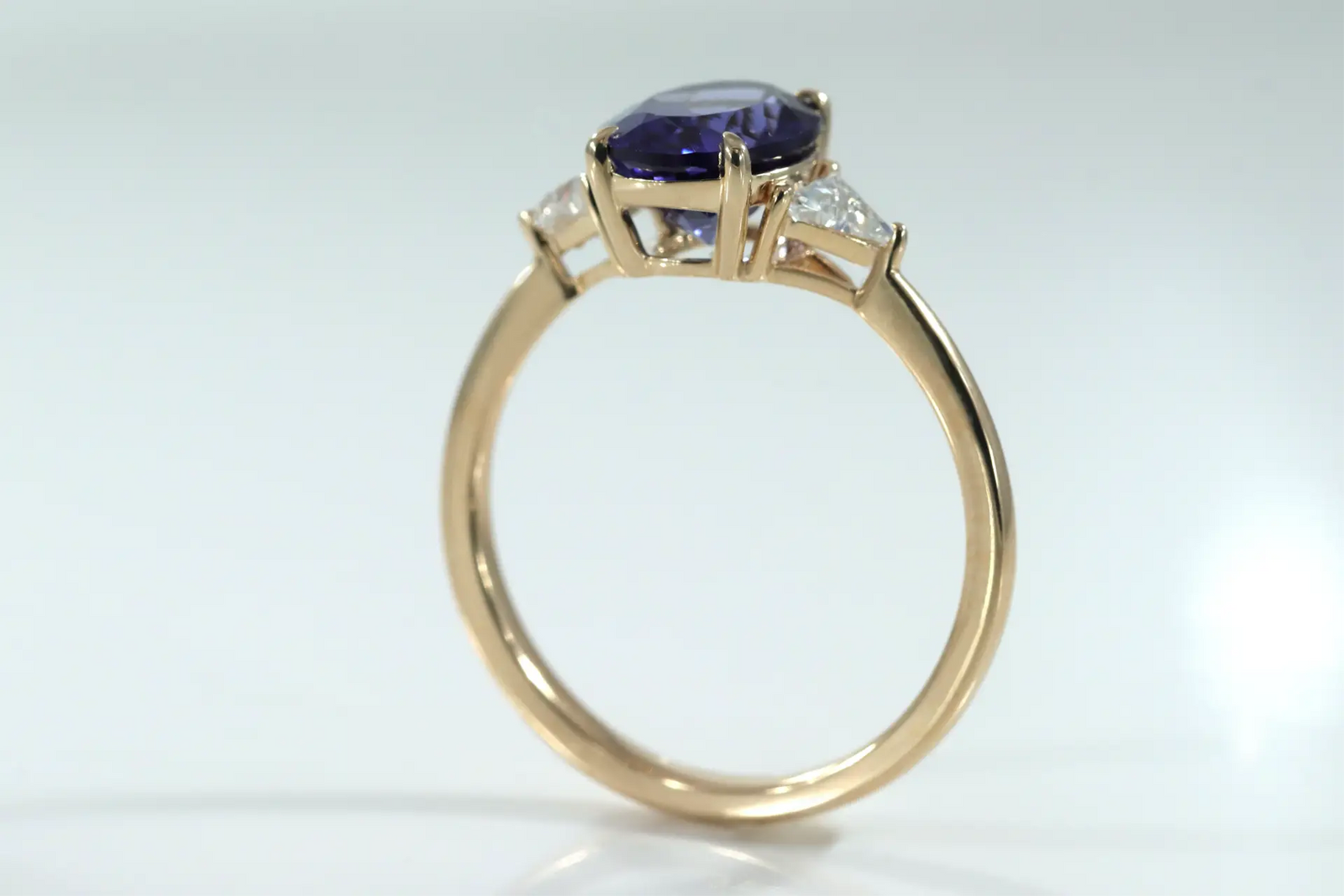 designer 14k yellow gold three stone engagement ring with 2 carat oval lab grown tanzanite center with lab grown diamond triangle sides at Quorri