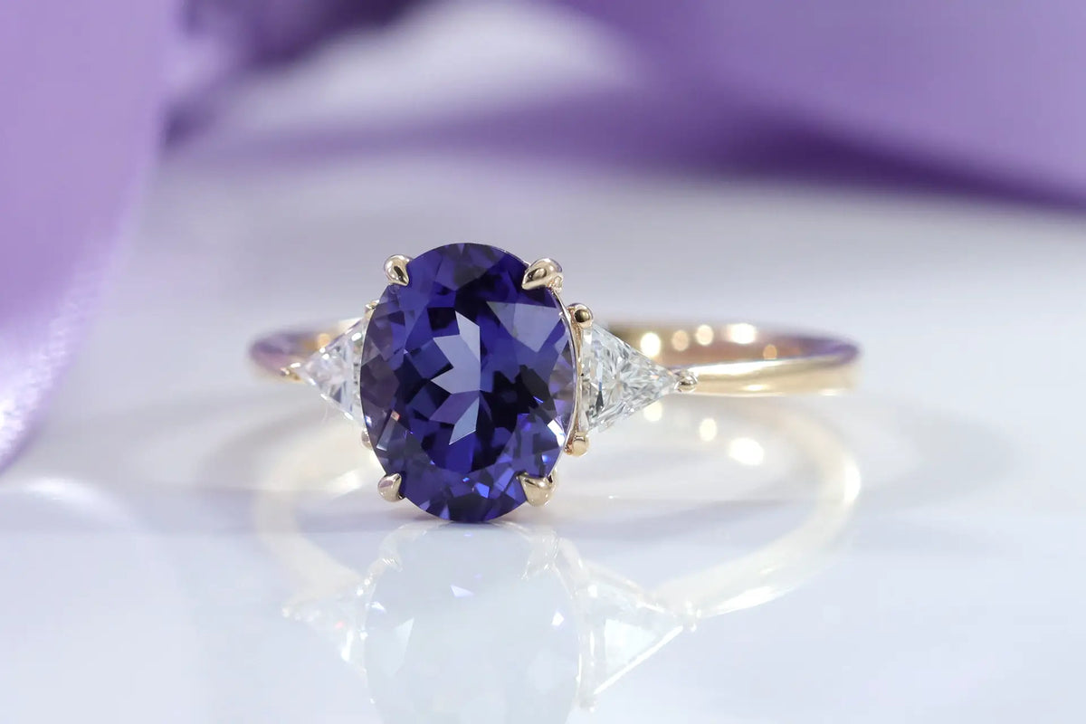 designer 14k yellow gold three stone engagement ring with claw prong 2 carat oval lab grown tanzanite center with lab grown diamond triangle sides at Quorri Canada