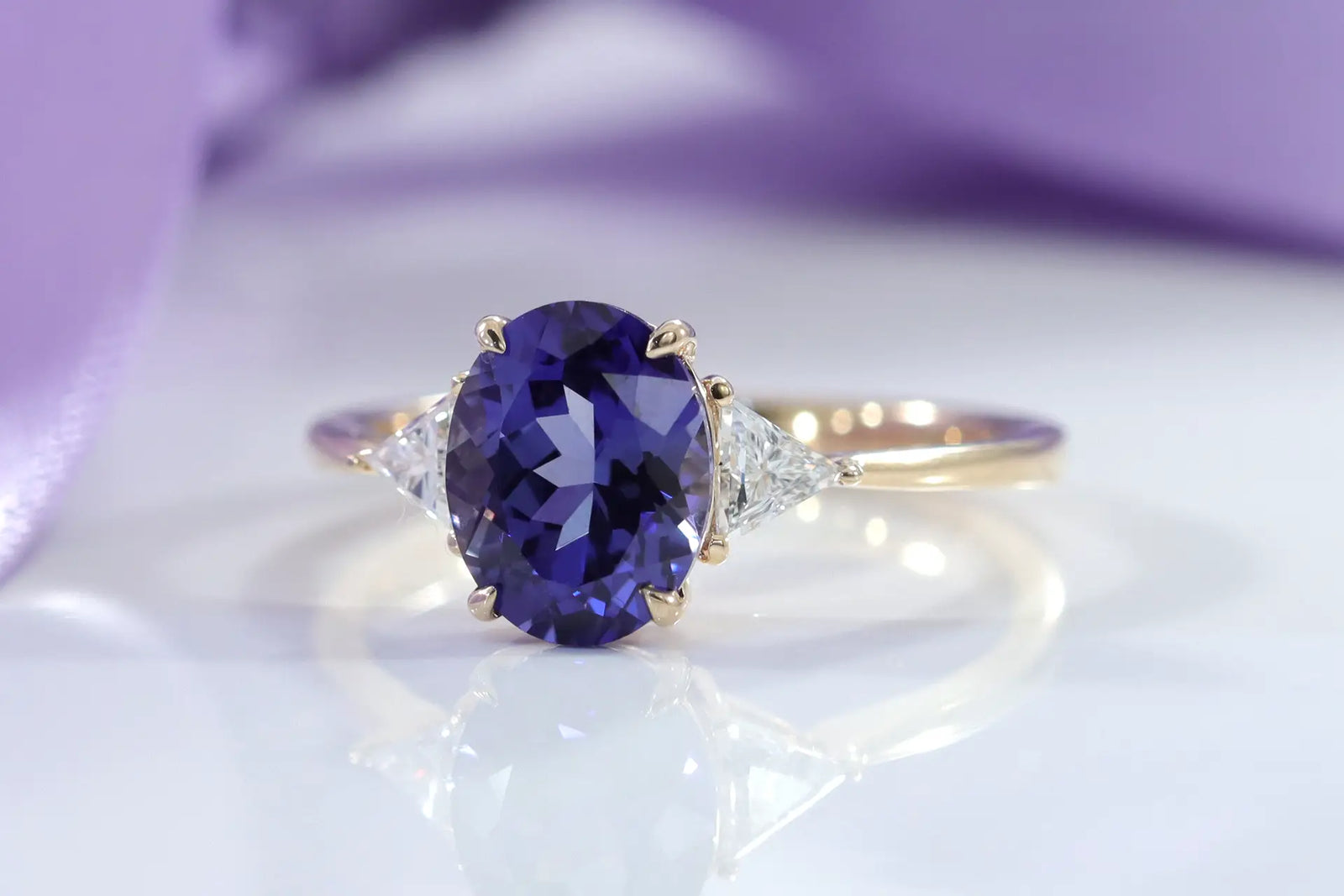 designer 14k yellow gold three stone engagement ring with claw prong 2 carat oval lab grown tanzanite center with lab grown diamond triangle sides at Quorri Canada