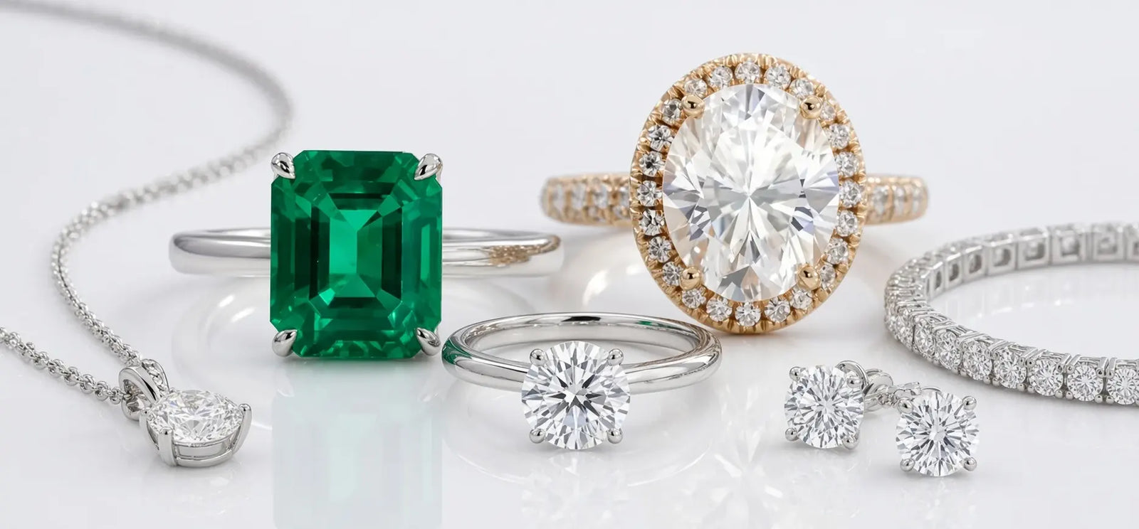 A collection of luxury jewelry from Quorri featuring a green emerald-cut diamond pendant, a yellow gold halo ring with a large round diamond, a silver solitaire ring, diamond stud earrings, a diamond bracelet, and a diamond necklace.