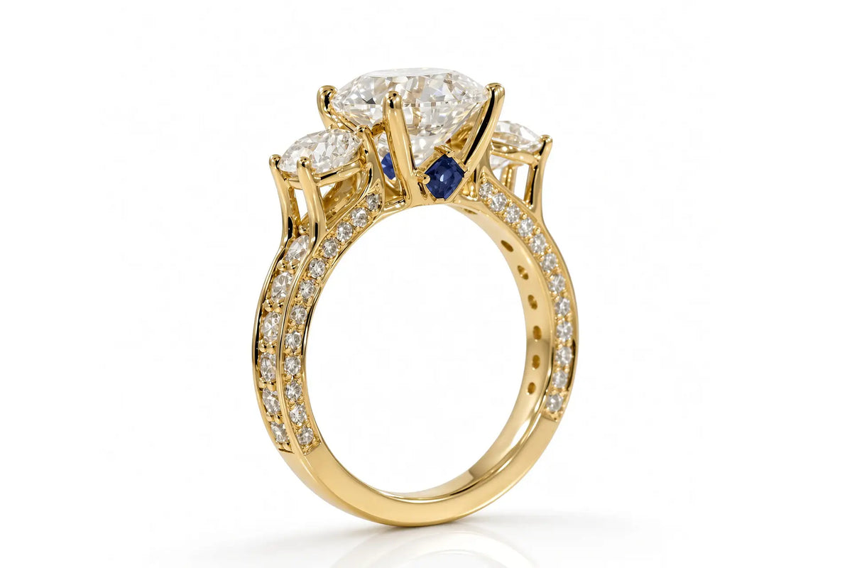 Yellow gold three-stone engagement ring with round brilliant diamond, pavé shoulders, and princess-cut sapphire blue accent